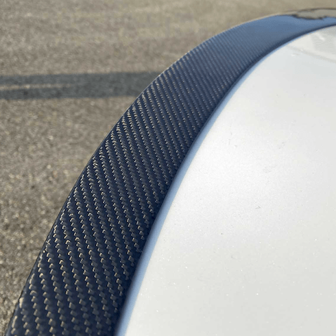 Nærbillede af carbon-spoilerens vævede kulfiber-struktur monteret på bagklappen af en hvid Tesla