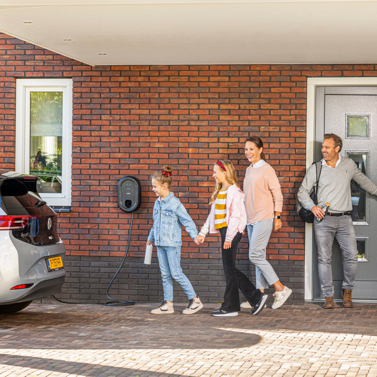 Familie verlaat huis met elektrische auto aangesloten op Ratio slimme laadpaal
