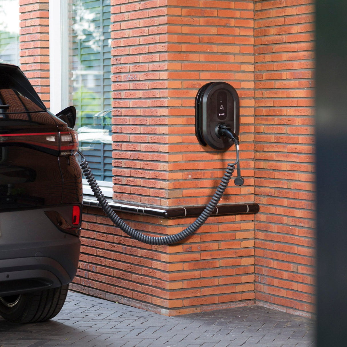 Ratio lader gemonteerd op een bakstenen muur, die een zwarte elektrische auto oplaadt