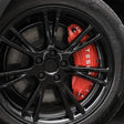 Rode remklauwhoezen met wit Tesla-logo op een zwarte velg.