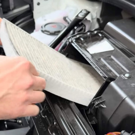 Een hand plaatst een koolstoffilter in de motorruimte van een VW ID.3/4/5/6/7.