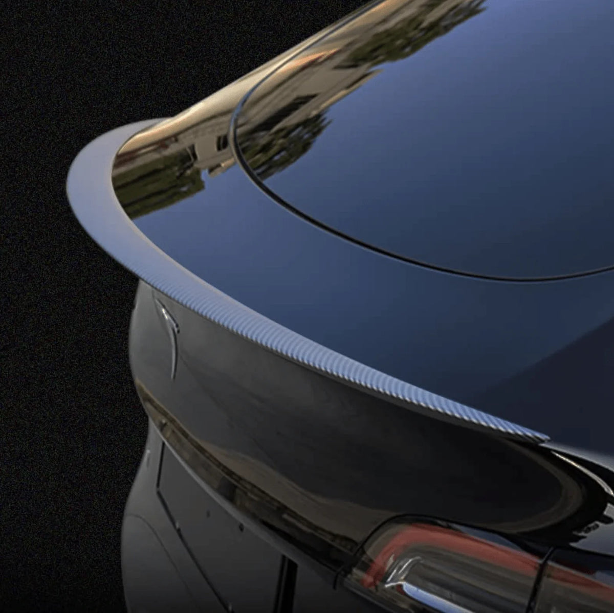 Nærbillede af performance-spoiler i ægte carbon monteret på bagklappen af en mørk Tesla